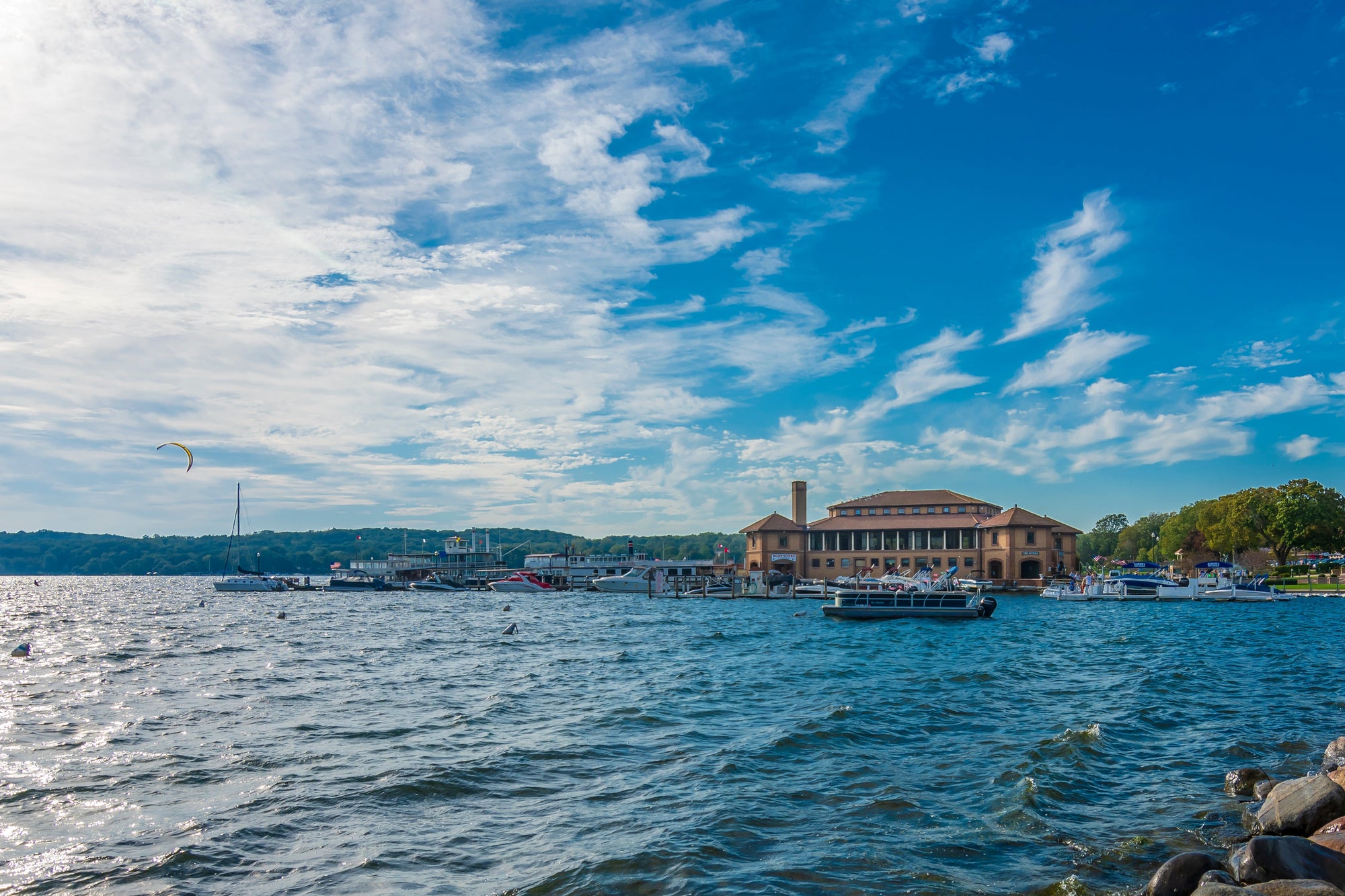Lakeside scene with a building and boats on a lake under a blue sky.